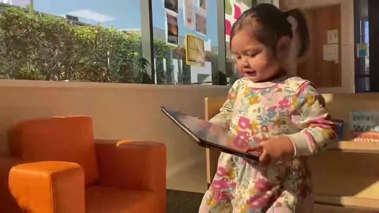 A child standing at a shelf, holding an open book