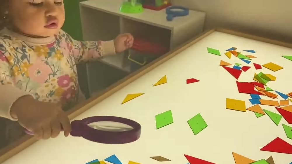 A child using a magnifying glass to explore coloured shapes on a light table
